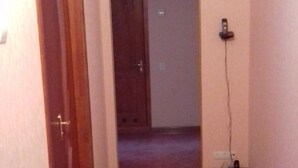 Um corredor com uma porta de madeira à esquerda, uma porta escura no final e uma tomada elétrica à direita.