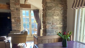 A rustic dining area with a stone wall, wooden beams, and a table with a dark tablecloth.