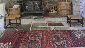 A rustic room with a stone fireplace, a wooden mantel, and a red patterned rug.
