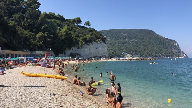 Una playa con gente, sombrillas y cielo despejado.