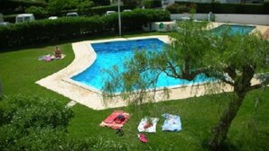 En swimmingpool omgiven av en gräsyta, med ett träd och en byggnad i bakgrunden.