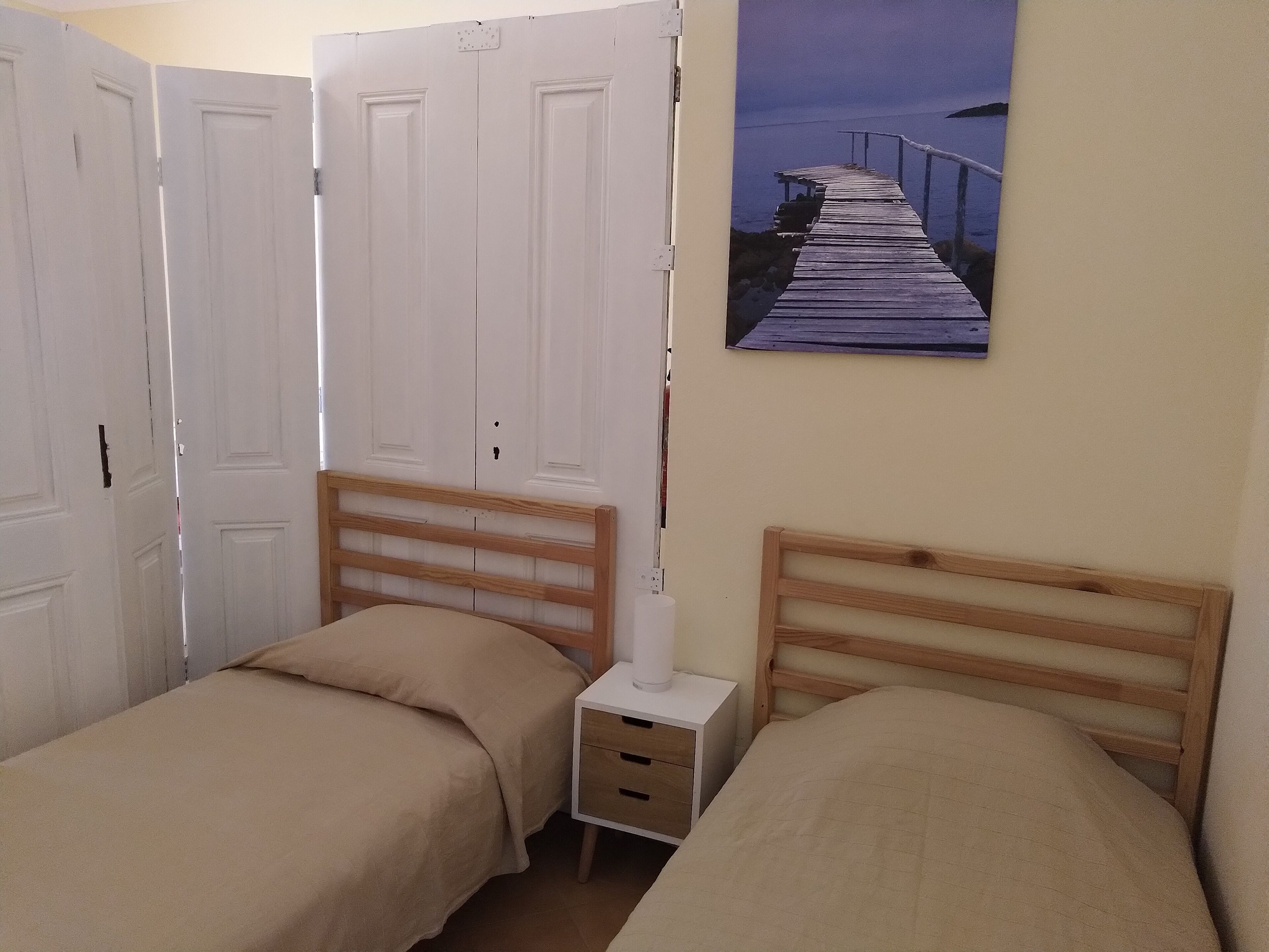 Une chambre avec deux lits simples, une table de chevet et un tableau accroché au mur représentant une jetée.