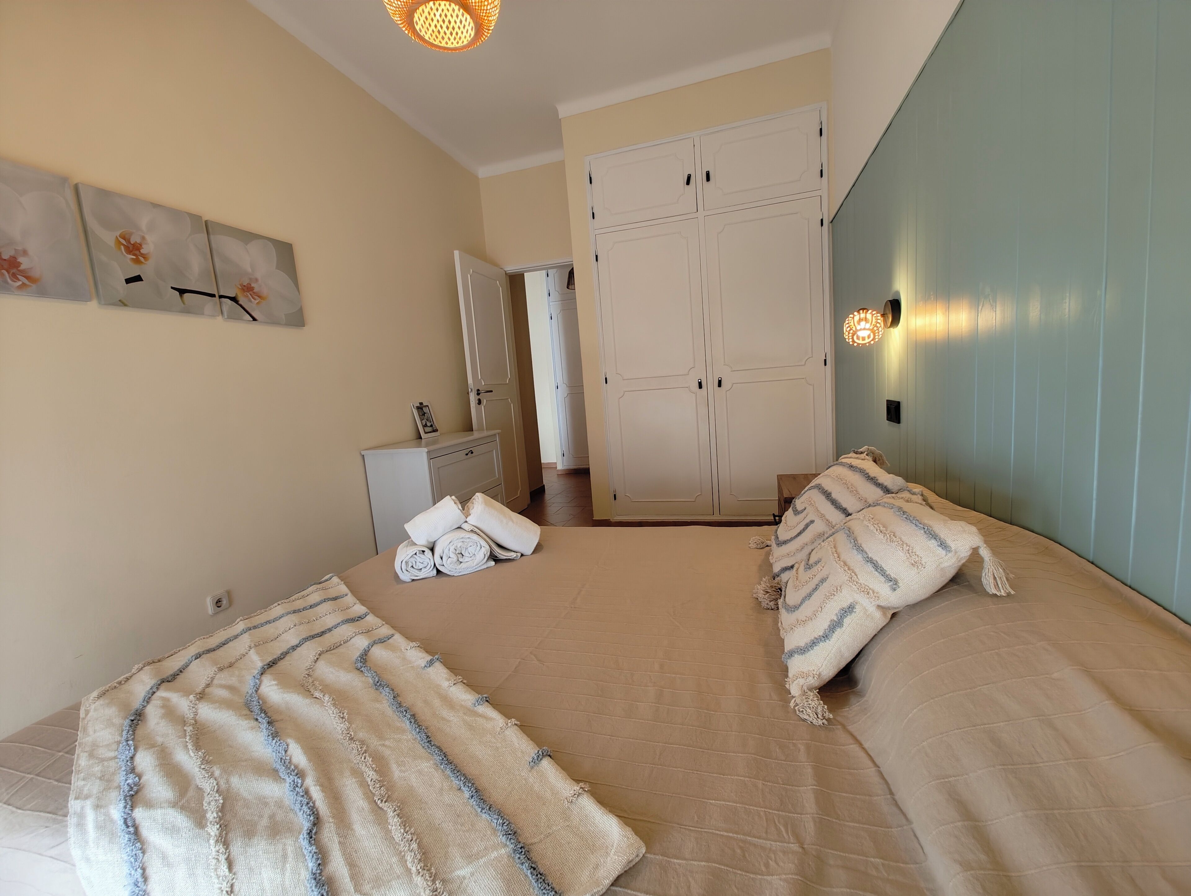 A bedroom with two beds, a wardrobe, a bedside table, and a wall-mounted light fixture.