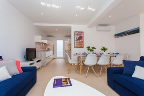 Un salon moderne avec un téléviseur, un canapé et un coin repas comprenant des chaises et une table.