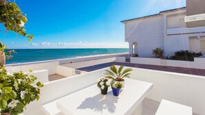 A terrace with a view of the sea, white furniture, and potted plants.