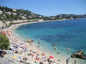 A beach with clear blue water, people sunbathing, and umbrellas.