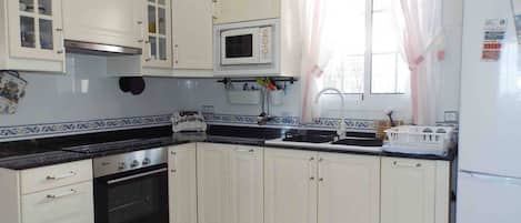 Una cucina con mobili bianchi, un forno a microonde, un forno, un lavello e un frigorifero.