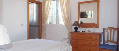 Una camera da letto con un letto, una cassettiera in legno, una sedia, uno specchio e una finestra con tende.