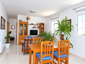 A dining area with a wooden table and chairs, a television, and potted plants.