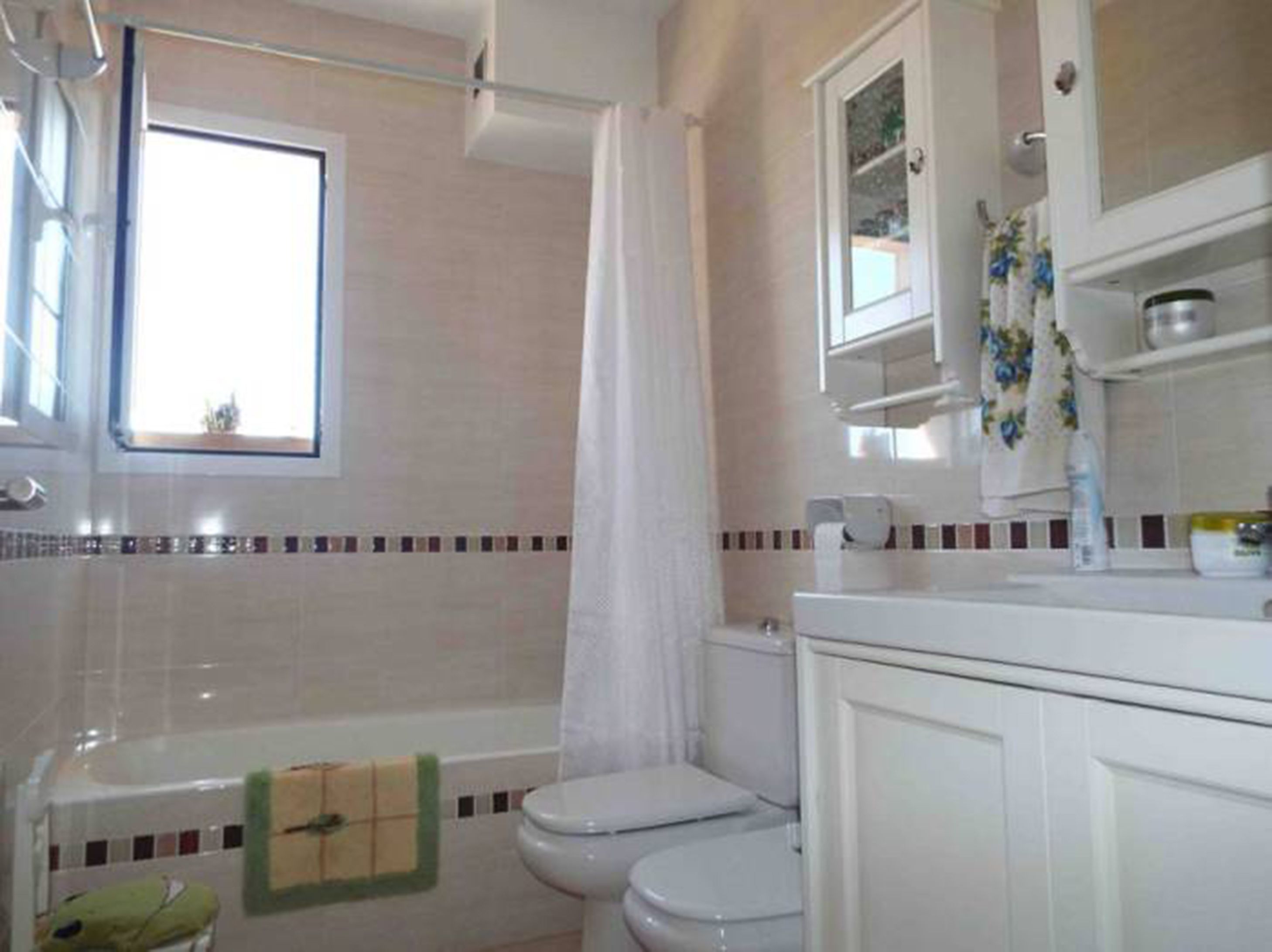 A bathroom with a bathtub, two toilets, a window, and a shower curtain.