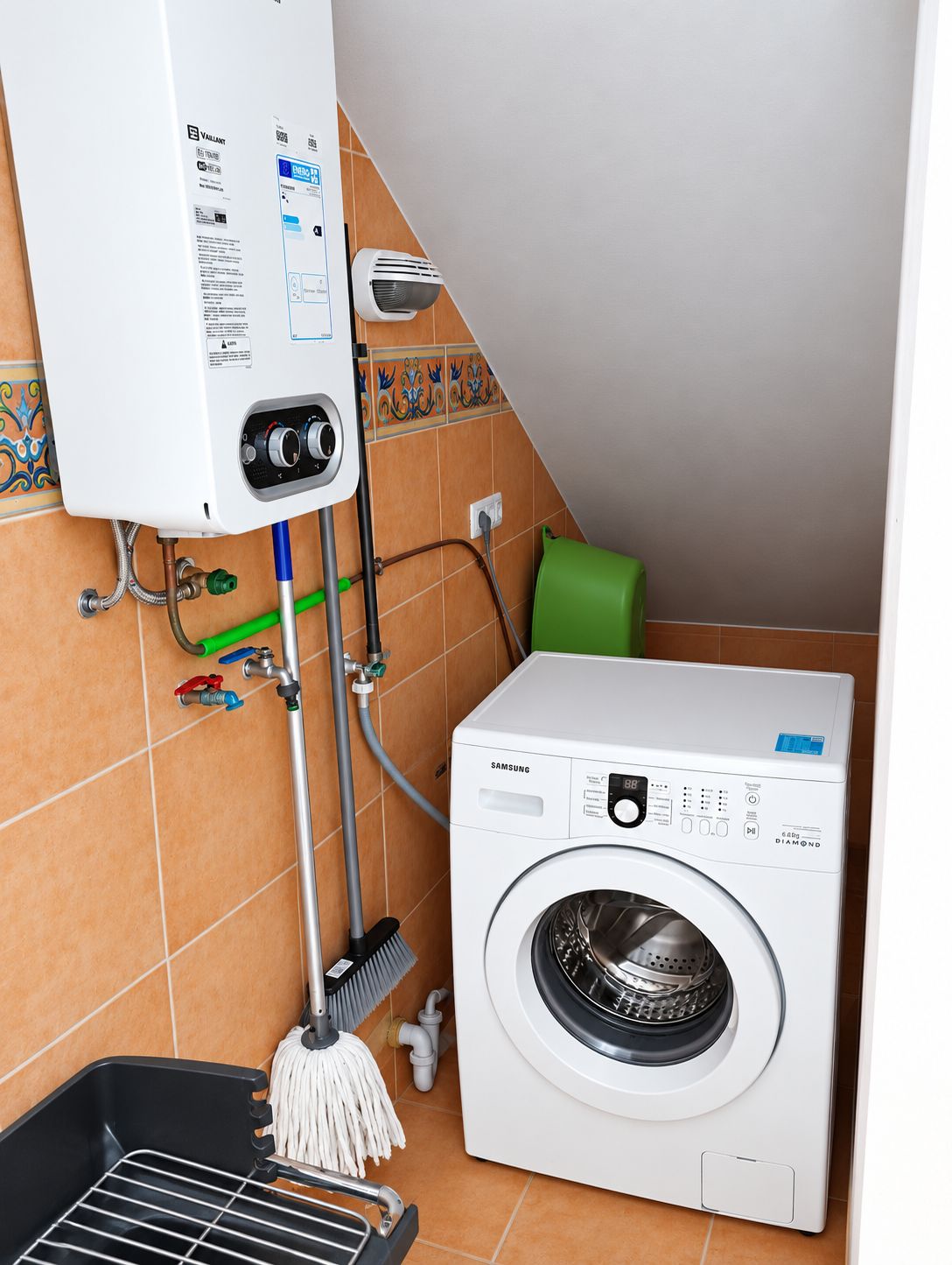 A bathroom with a white washing machine, a water heater, and a mop.