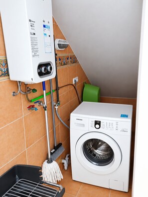 Ein Badezimmer mit einer weißen Waschmaschine, einem Warmwasserbereiter und einem Mopp.