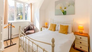 A bedroom with a bed, bedside tables, a chair, a radiator, and a window with curtains.