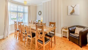 A dining area with a wooden table and chairs, a black leather sofa, a small side table, and a wall clock.