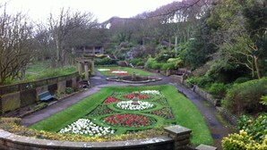 A formal garden with symmetrical flower beds, a central fountain, and a stone bench.