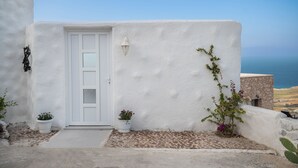 Een wit bekleed gebouw met een witte deur, planten in potten en uitzicht op zee.