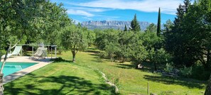 A backyard with a swimming pool, lounge chairs, and a view of mountains. - Wooden house in a green setting (Fuveau)