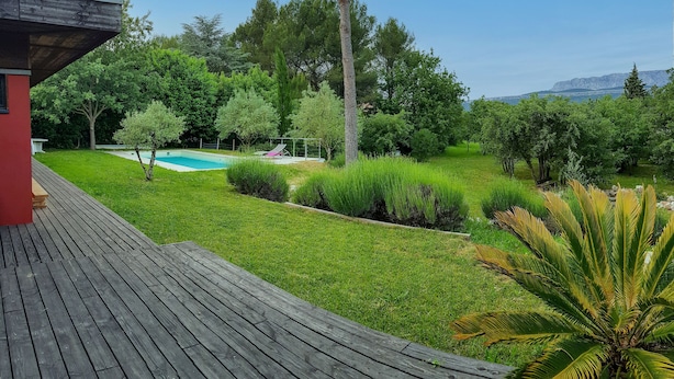 Un pontile in legno che conduce a una piscina circondata da vegetazione lussureggiante e alberi.