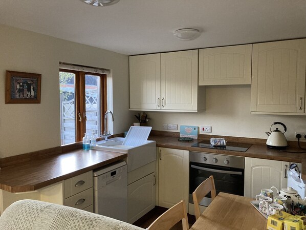 A compact kitchen with white cabinets, a dishwasher, an oven, and a window with a view of greenery.