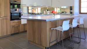A modern kitchen with wooden cabinets, stainless steel appliances, a large island with bar stools, and pendant lighting. - Luxury renovation of an ancient stone barn in a medieval bastide village (Montcabrier)