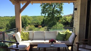A covered outdoor seating area with a wooden bench, a sofa with cushions, and a table. - Luxury renovation of an ancient stone barn in a medieval bastide village (Montcabrier)