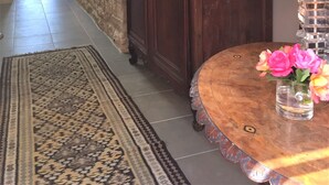 A hallway with a stone wall, a wooden cabinet, a patterned rug, and a round table with a vase of flowers. - Luxury renovation of an ancient stone barn in a medieval bastide village (Montcabrier)