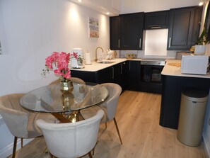 Una cocina moderna con armarios oscuros, una mesa de comedor con superficie de vidrio y un cubo de basura.