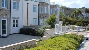 A row of white buildings with balconies, a paved courtyard, and surrounding greenery. - Stunning Luxury Apartment In Carbis Bay, St Ives Close To The Beach with Parking (Carbis Bay, St Ives)