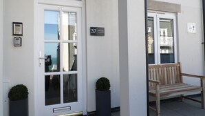 A white building with a large arched door, a bench, and a small potted plant. - Stunning Luxury Apartment In Carbis Bay, St Ives Close To The Beach with Parking (Carbis Bay, St Ives)