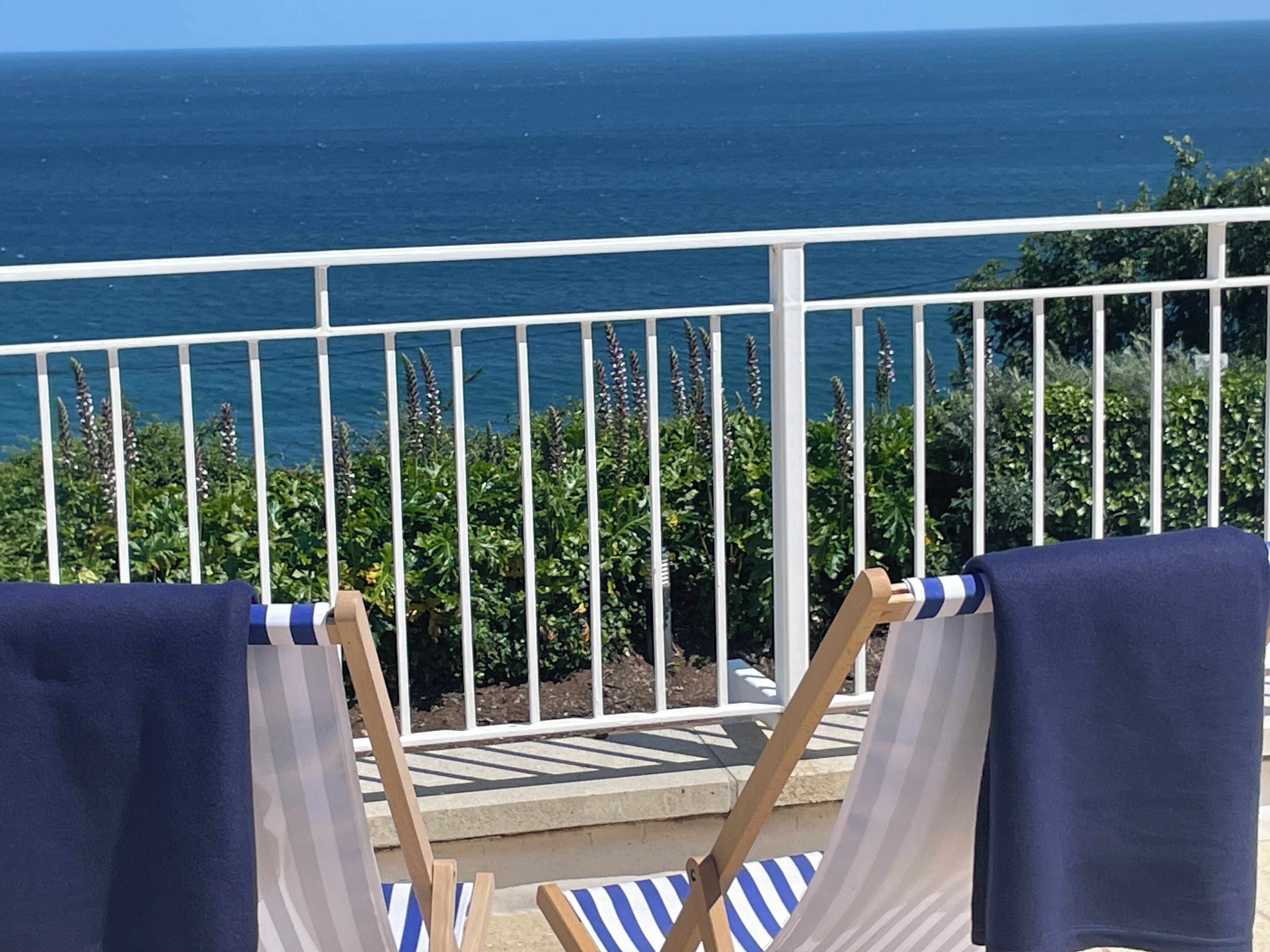 A balcony with a view of the ocean, two chairs with towels, and a railing.