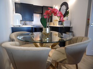 A modern kitchen with dark cabinets, a round glass table, and beige chairs.