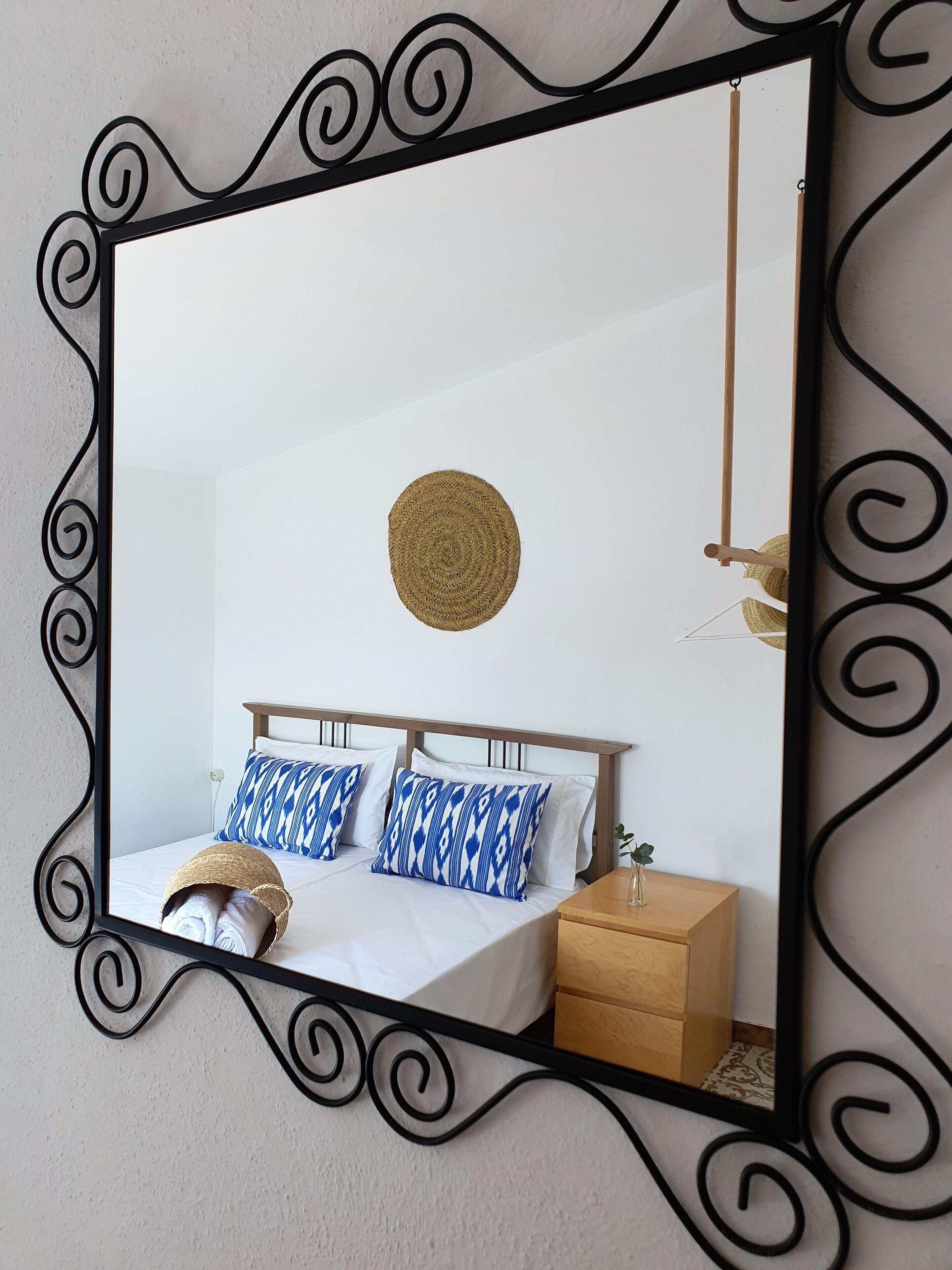 A bedroom with a bed, two pillows, a bedside table, and a mirror with a decorative frame.