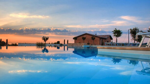 A serene pool area with a sunset view, a brick building, and palm trees. - Le Orchidee Luxury Country Villa with pool just minutes from the Riviera (Roncofreddo)