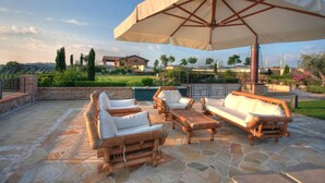 An outdoor patio with stone flooring, wooden furniture, and a large umbrella providing shade. - Le Orchidee Luxury Country Villa with pool just minutes from the Riviera (Roncofreddo)
