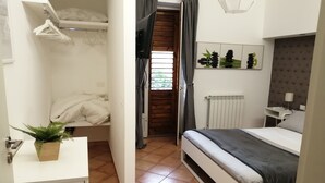 A bedroom with a bed, a bedside table, a hanging light, a radiator, and a window with curtains.