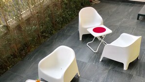 A patio area with four white plastic chairs and a small table, each with a red circular cushion. A tray with snacks and drinks is placed on the table.