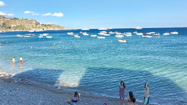 A beach with clear blue water, boats, and rocky terrain.