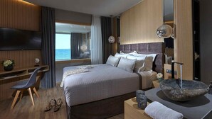 A modern hotel room with a large bed, a desk, a chair, and a view of the sea. - Seafront Apt, beachfront, quiet & central with infinity pool (Limenas Chersonisou)