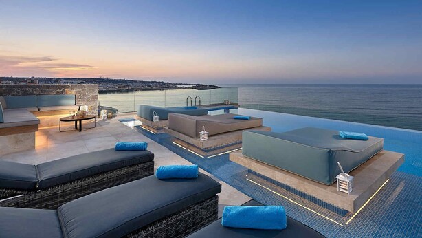 An infinity pool with a view of the sea, outdoor seating, and a glass railing. - Seafront Apt, beachfront, quiet & central with infinity pool (Limenas Chersonisou)