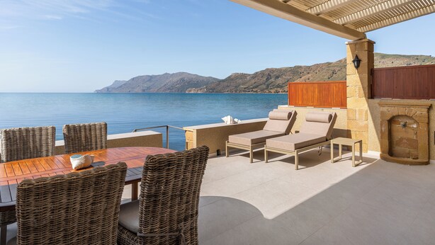 An outdoor patio with wicker furniture, a stone fireplace, and a view of the sea and mountains.