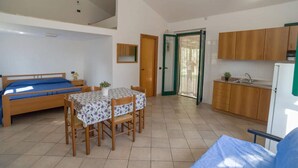 A compact room with a bed, a dining table with chairs, a small kitchen area, and a door leading to another room.
