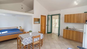 A compact living space with a bed, a dining table with chairs, a kitchenette, and a door leading to an outdoor area.