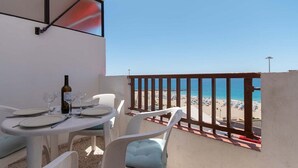 Ein Balkon mit Tisch für zwei Personen, mit Blick auf einen Strand.