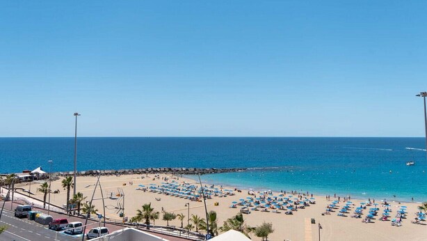 Ein Strand mit mehreren Reihen von Sonnenschirmen und Liegestühlen, einem strahlend blauen Himmel und dem Meer.