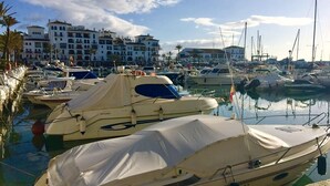 Un puerto deportivo con varios yates amarrados, rodeado de edificios con balcones y un cielo despejado.