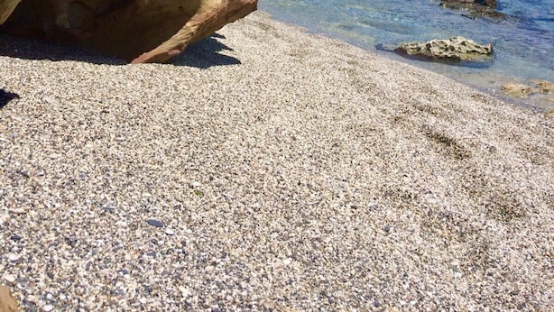 Una costa rocosa con agua azul cristalina y una playa de guijarros.