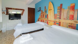 Een hotelkamer met twee bedden, een televisie op een dressoir en een kleurrijke muurschildering van een surfboard op de wand.