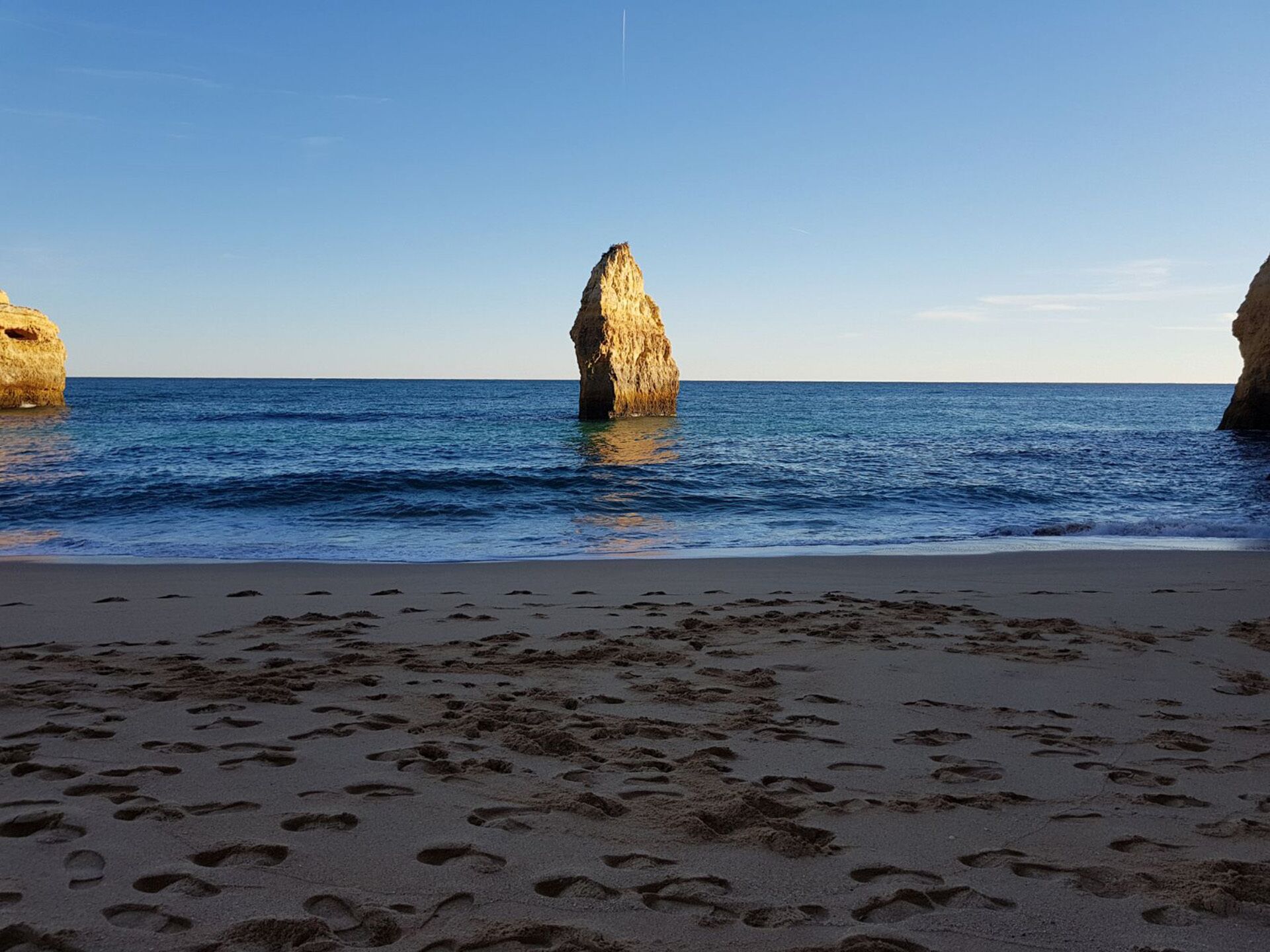 A beach with footprints leading to a rocky outcrop in the water.