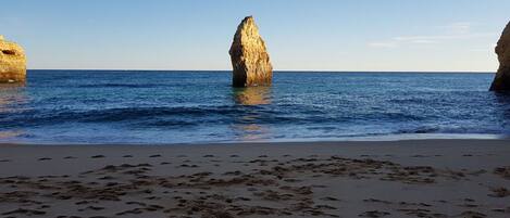 A beach with footprints leading to a rocky outcrop in the water.