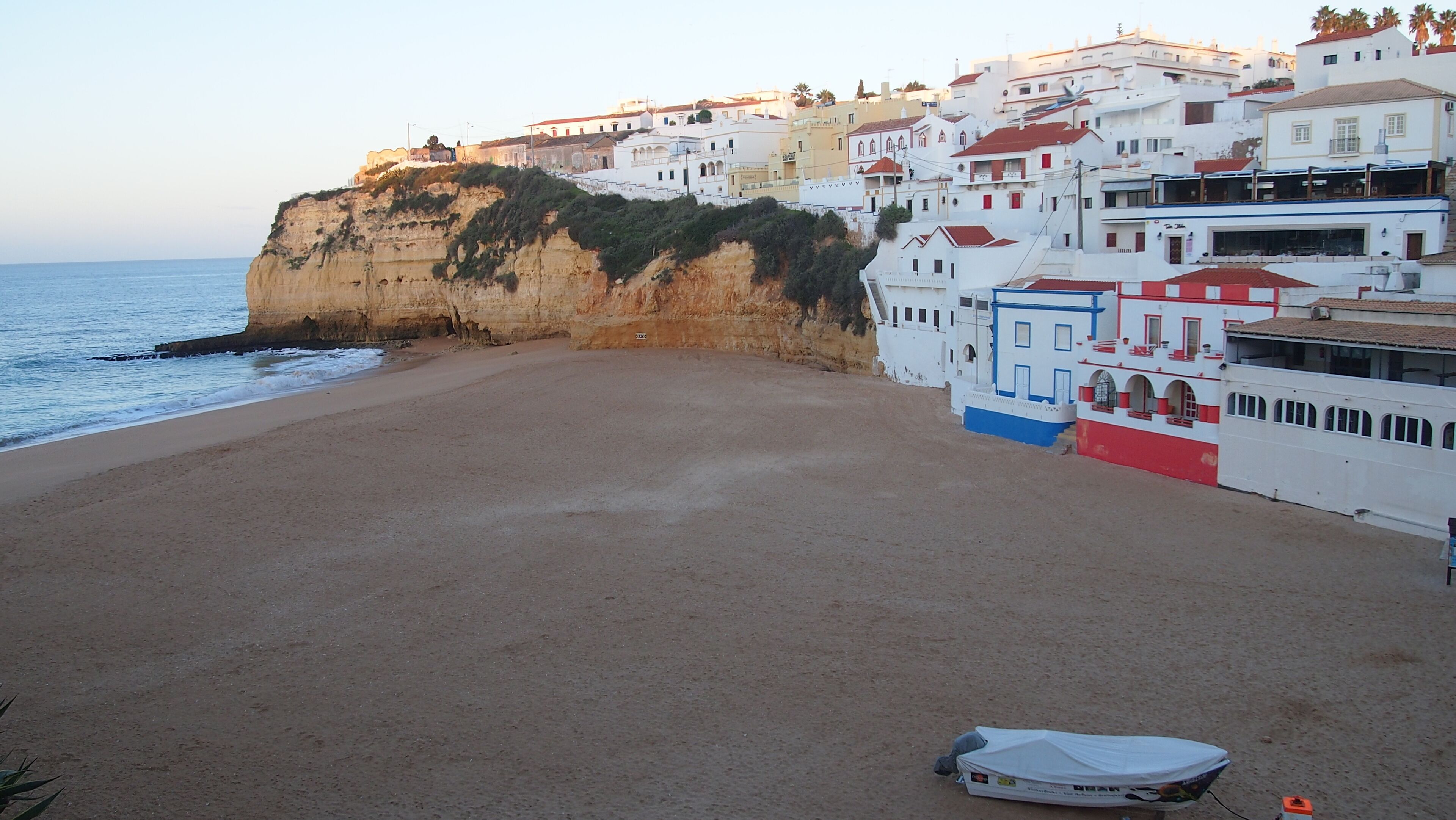 A beach with a cliff and buildings in the background.